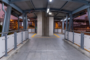 Obraz premium Modern urban pedestrian walkway at dusk with minimal people and illuminated signage in a bustling cityscape