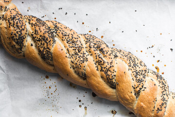 Overhead view of braided challah dough with sesame on a parchment lined baking sheet, top view of twisted challah loaf with black sesame on a baking tray, process of making challah