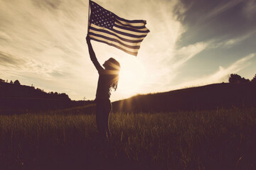 A person holds an American flag in a field, under a clear blue sky, symbolizing patriotism and freedom.