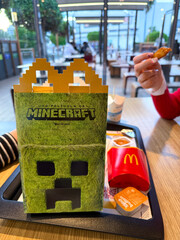Naklejka premium McDonald's themed food box in Minecraft style with iconic character, colorful french fries and nuggets on wooden table, fast food concept
