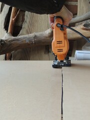 using a jigsaw to cut thin sheets of plywood or wood or thick sheets of cardboard along a line, carpentry workshop with craft materials and hand tools, jigsaw cutting in a straight line