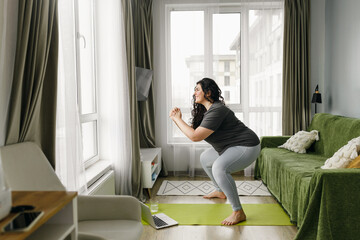 Losing weight online fitness program concept. Plus size woman in sports clothes training at home,...