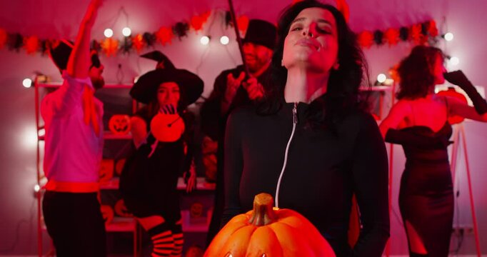 Happy Halloween holiday funny demon devil woman dancing with friends wearing costumes for dress ups party night event, playing spooky horror cosplay look, garland red light decor atmosphere fun