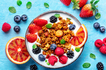 Granola with yogurt and fresh fruit. Organic gourmet muesli, overhead flat lay shot on a blue background, with ingredients