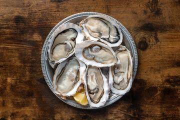 Fresh raw oysters on ice, overhead flat lay shot on a rustic wooden table, with lemon