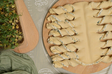 Top view close up twisted dough strips on wooden board. Green towel, microgreens sprouts on kitchen table. Home cooking baking puffs