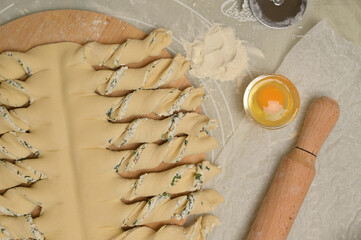 Top view close up twisted dough strips on wooden board. Cutter, egg, rolling pin on kitchen table. Home cooking baking puffs