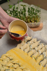 Close up woman's hands smears yolk on the twisted dough strips with a brush. Red small bowl with egg. Rolling pin, microgreens sprouts on kitchen table. Home cooking baking puffs