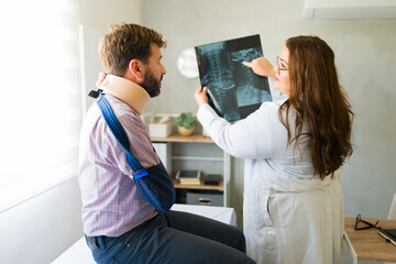 Caring female doctor explaining x-ray results to a male patient wearing neck brace and arm sling...
