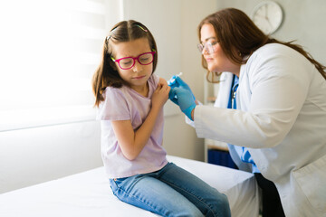 Plus size pediatrician vaccinating a little girl in her doctor's office, promoting children's...