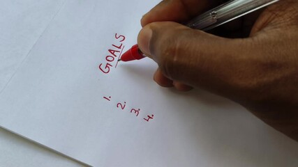 Closeup of hand with red pen underline word goals written on white paper. Ambition, planning, setting goal, aspirations, personal development and motivation concept.