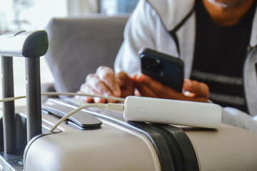 Cropped image of a South Asian man waiting in airport lounge charging his phone using power bank before departure. Focus on the foreground.