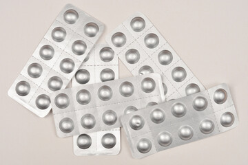 A flat lay of scattered silver blister packs with round indentations for pills, arranged...