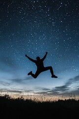 Silhouette of person jumping against a starry night sky in a field setting