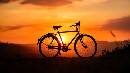 Fototapeta premium Silhouette of bicycle at sunset on a countryside hilltop with vibrant orange sky