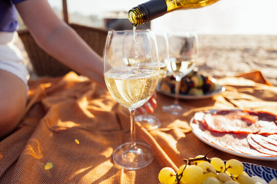 Close-up of a glass of champagne on a picnic mat. The cup is filled with sparkling wine outdoors on the beach. Delicious snacks and drinks by the sea.