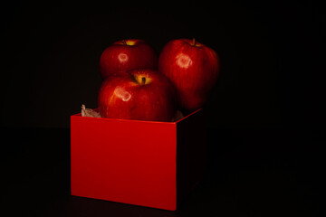 Red apples and red boxes on a black background, with dim lighting to simulate a chiaroscuro effect © Migeli Barrios