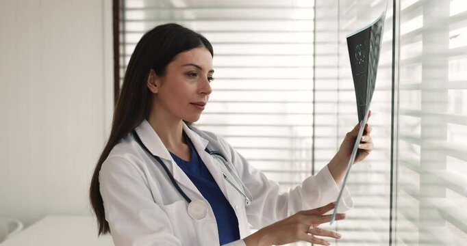 Radiologist or neurologist woman examining brain scan MRI image, standing in workplace, analyzing medical scan for diagnosis or treatment planning, interpreting x-ray, monitoring disease progression