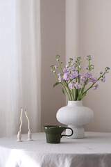 A beautifully serene table display that features delicate flowers in ceramic vase, an elegant green mug, and candles.