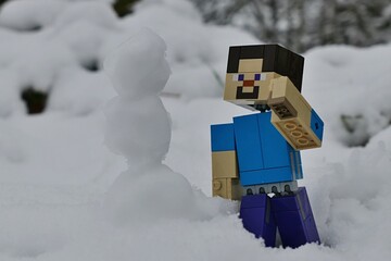 Naklejka premium LEGO Minecraft large figure of Steve just build a slim snowman in snow covered forest. 