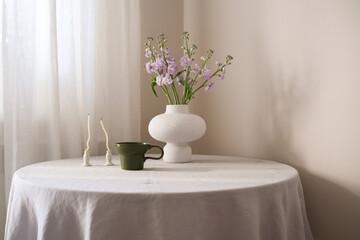 A beautifully serene table arrangement featuring vibrant flowers, elegant green cup of coffee, and minimalistic candles on round table.