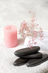 Bright spa still life with white towel, pink candle, delicate flowers, and dark massage stones. Airy, soft light creates a calm, relaxing, and feminine atmosphere. Ideal for wellness themes.