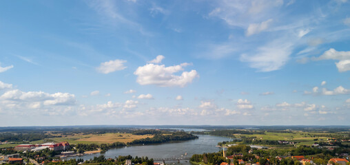Panoramic view of a serene landscape with a river, fields, and scattered clouds under a bright blue...