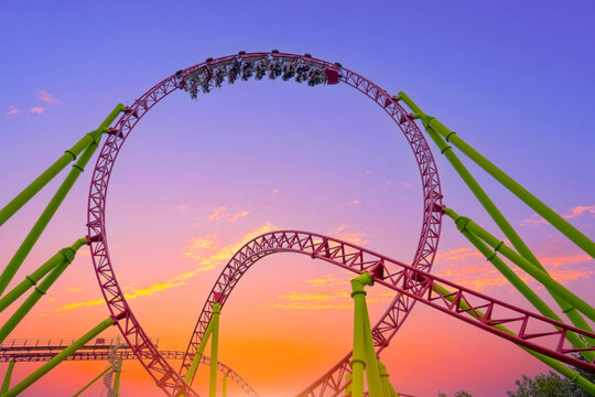 Thrilling roller coaster racing through twists and loops at lively amusement park, capturing the energy, excitement, fun of high speed theme park experiences, orange light against the sunset sky