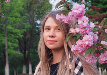 Fototapeta premium Young woman posing among blooming pink flowers in a botanical garden during springtime