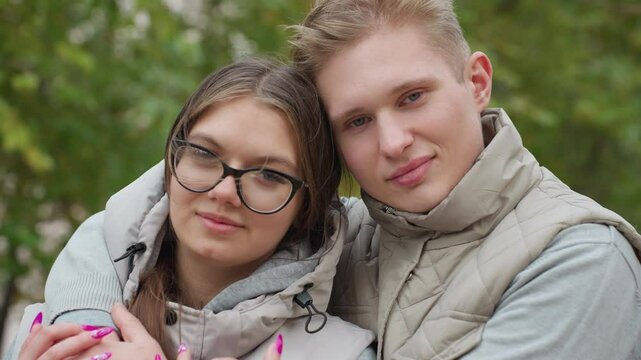 Wonderful moment of couple standing closely outdoors in matching outfits, sharing subtle smiles while trees sway gently in background