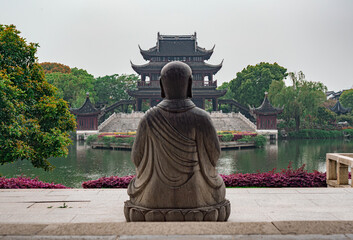 Obraz premium Serene view of a stone Buddha facing a traditional pavilion near a tranquil lake in a Chinese garden