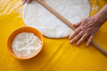 Old woman rolling raw dough with rolling pin.