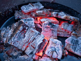Glowing embers of burning wood in a fire pit, texture of the charcoal and ashes in grill