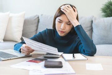 Debt and financial concept, stressed asian young woman have a headache while female calculate expenses, income and expenses, looking bills of credit card for payment or payday on table at home office.