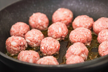 Uncooked meatballs start to sizzle in a hot pan.