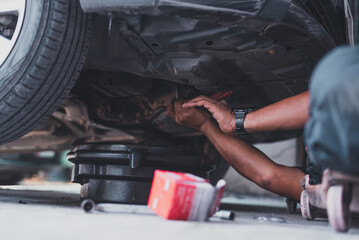 A mechanic lies on a creeper beneath a vehicle, performing maintenance or an oil change using tools...