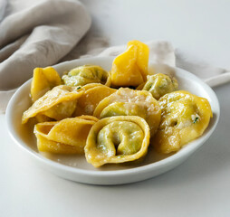 Plate of Italian tortellini filled with spinach and ricotta cheese, served with butter and sage sauce. Elegant presentation on a white plate, with a light napkin, in a rustic and appetising style.