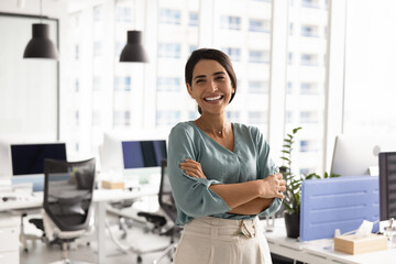 Happy successful female Latin businesswoman posing in office workspace alone, looking at camera,...