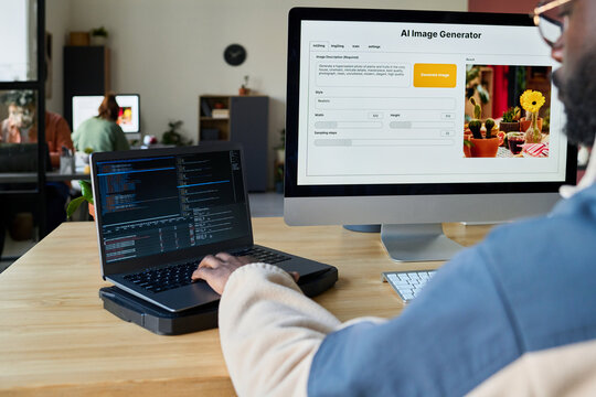 Focus on two desktop computers and hand of young male programmer typing on laptop keypad while decoding data