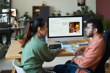 Side view of young intercultural designers using and discussing possibilities of new AI image generator in front of computer screen