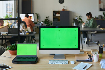 Two computers with chromakey screens standing on desk against group of coworkers networking in modern spacious office