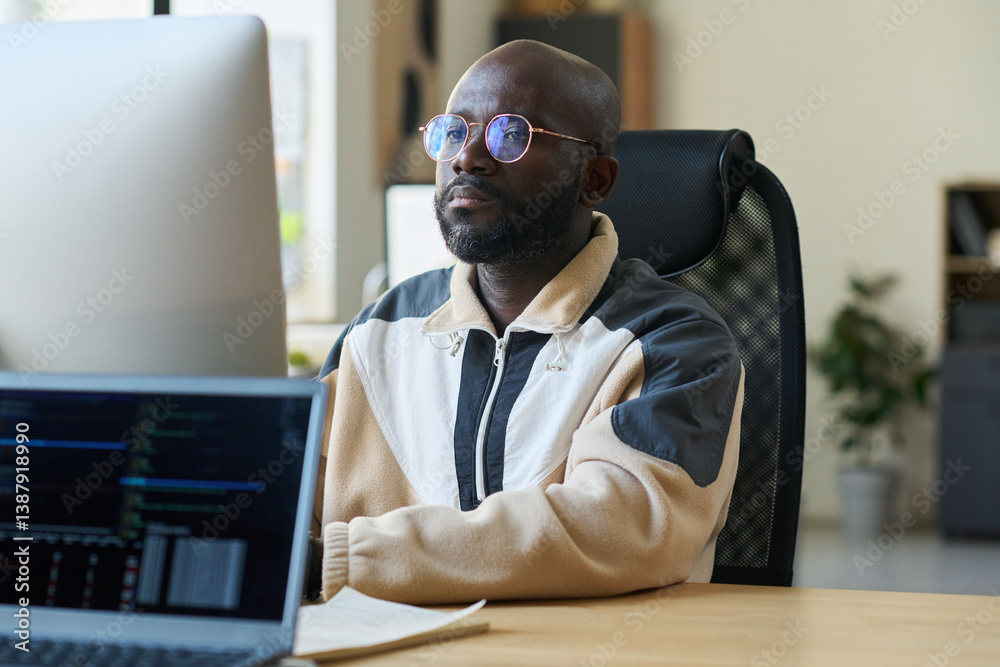 Poster Young serious man concentrating on reading information on computer screen while decoding it by his workplace