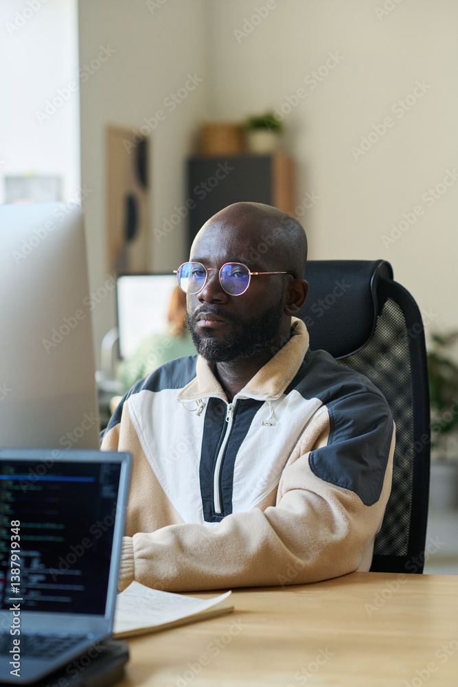 Aufkleber Serious young African American male designer or programmer in eyeglasses sitting in front of computer and looking at screen