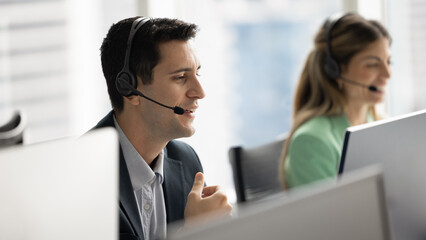 Positive Hispanic telephone support employee man speaking to customer on audio call, using headset with mic and computer monitor, giving instruction, advice, technical help to client. Banner shot