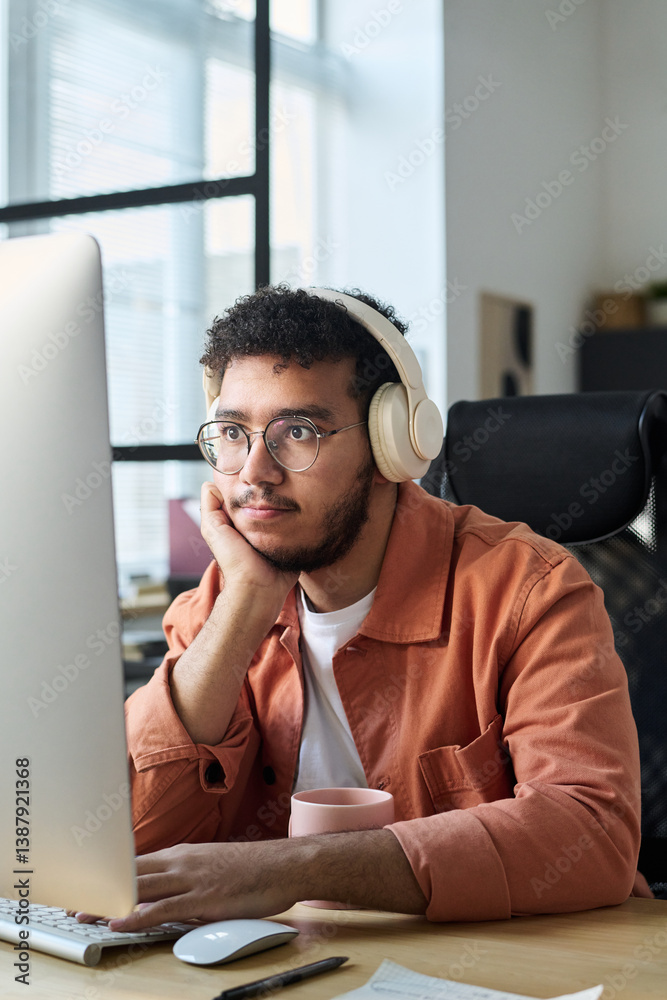 Aufkleber Young serious male programmer in headphones using desktop computer and looking at screen while generating new content