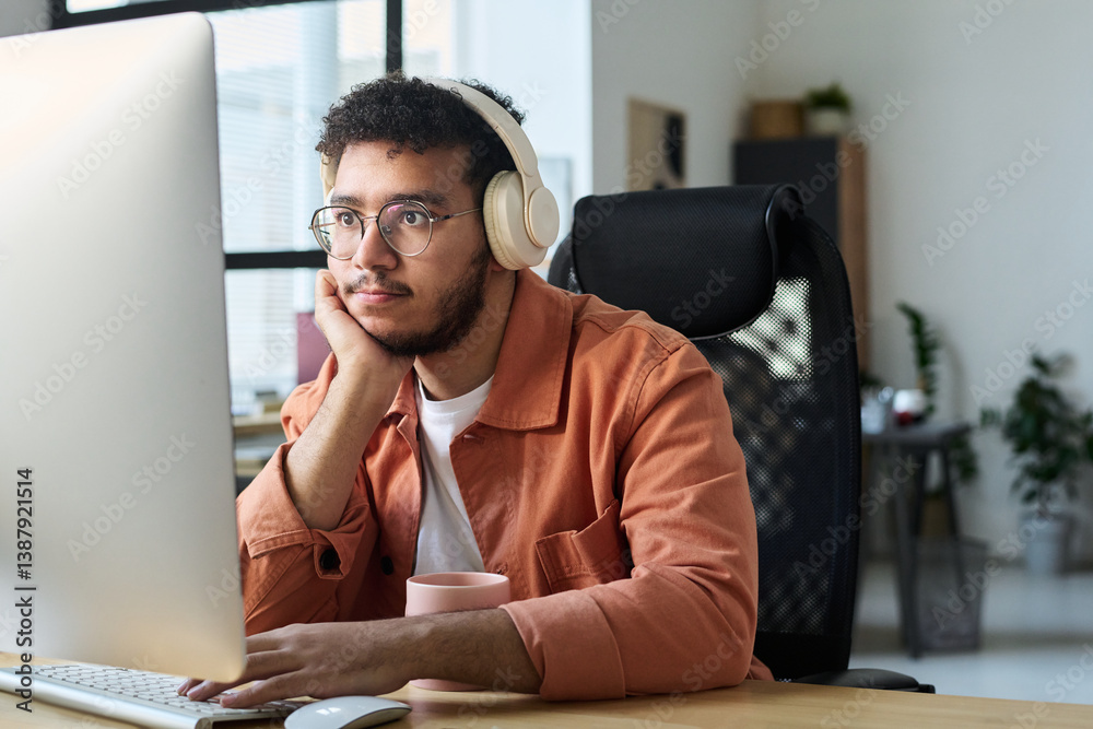 Aufkleber Young serious man in headphones looking at computer screen and keeping hand on keypad while watching online video