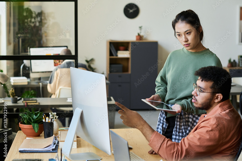 Poster Young male programmer pointing at computer screen while discussing ways of decoding data with female colleague at meeting