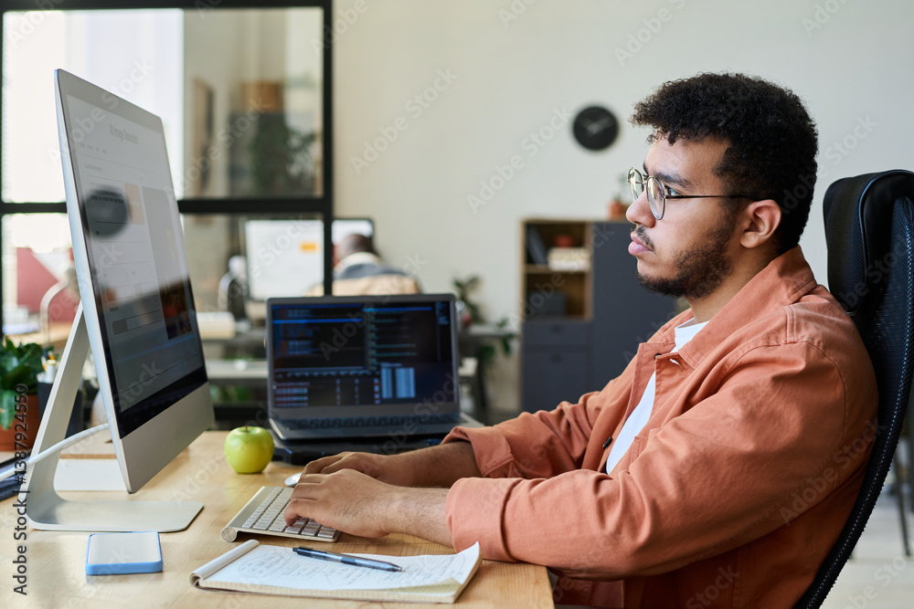 Poster Young male designer creating new content with AI image generator while sitting in front of computer and typing on keypad
