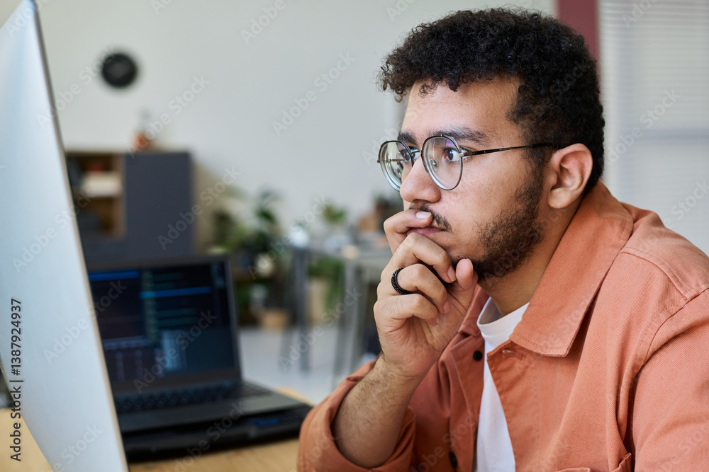 Aufkleber Young pensive male programmer keeping hand by his mouth and looking at computer screen while decoding information