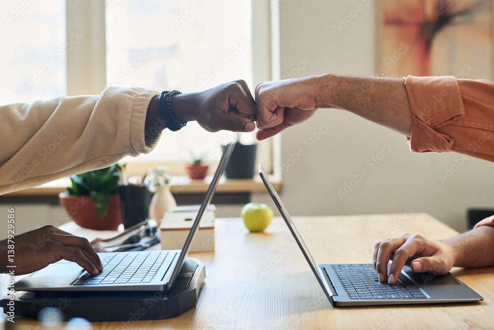 Aufkleber side view of punch bump of two young intercultural male programmers over laptops during work over ne